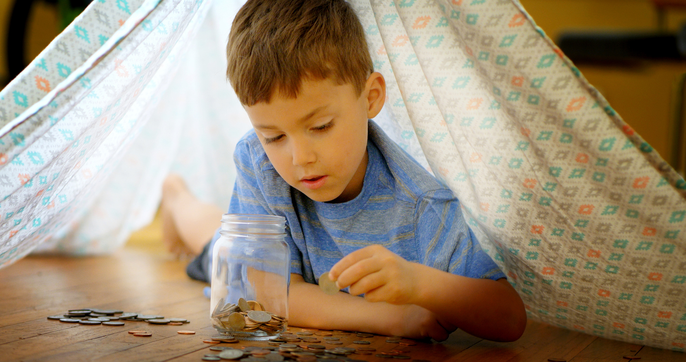 Little boy adding coins to jar.