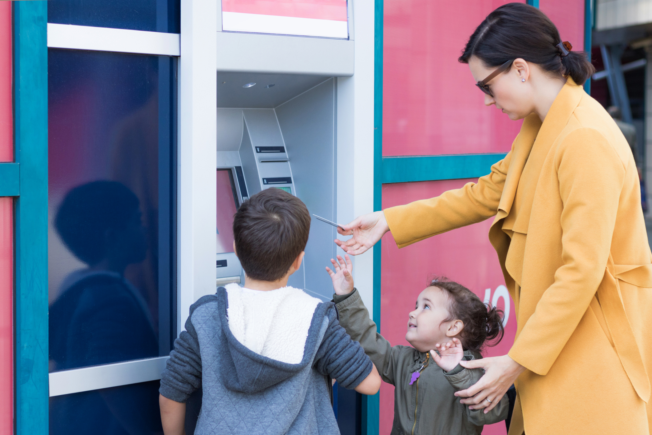 Mother and children withdrawing money from ATM machine.