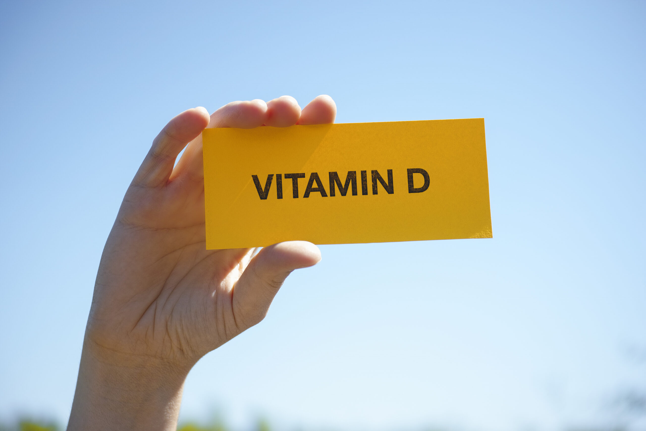 Hand holds piece of paper with Vitamin D against sunny blue sky