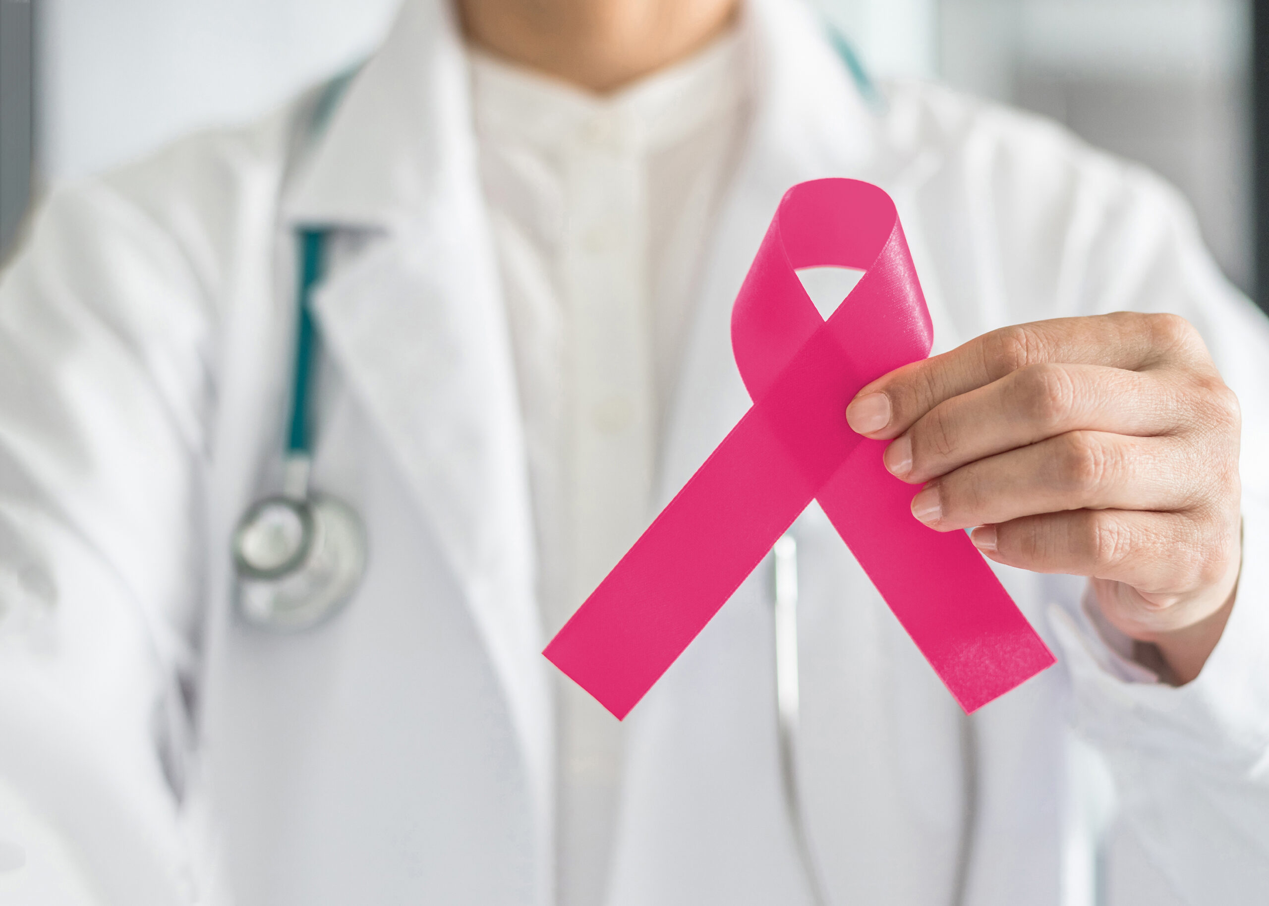 Pink ribbon for breast cancer awareness in doctor's hand, symbolic bow color for raising awareness campaign on women (female)  patient living with breast tumor illness