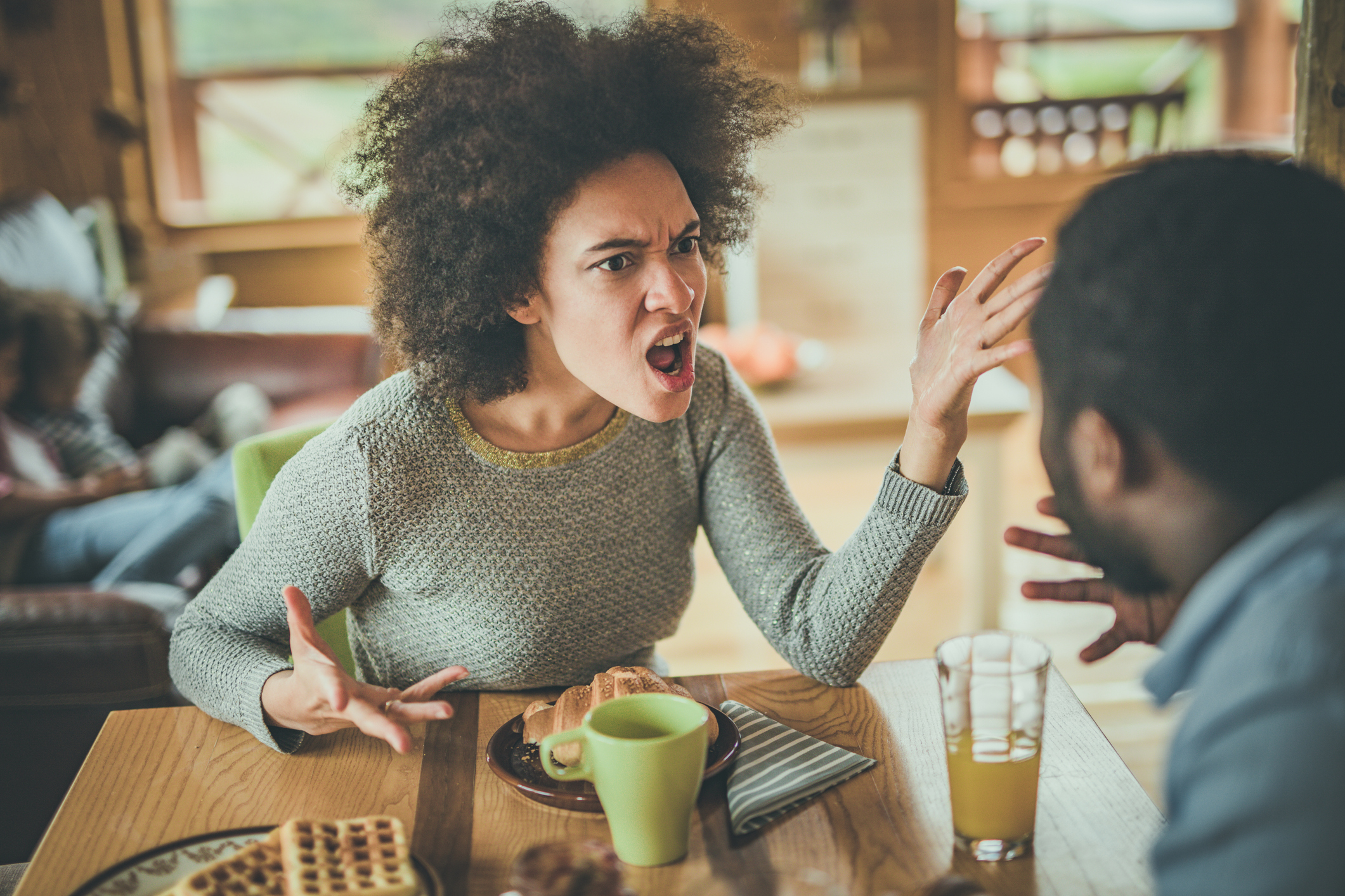 Angry African American woman arguing with her husband at dining table.