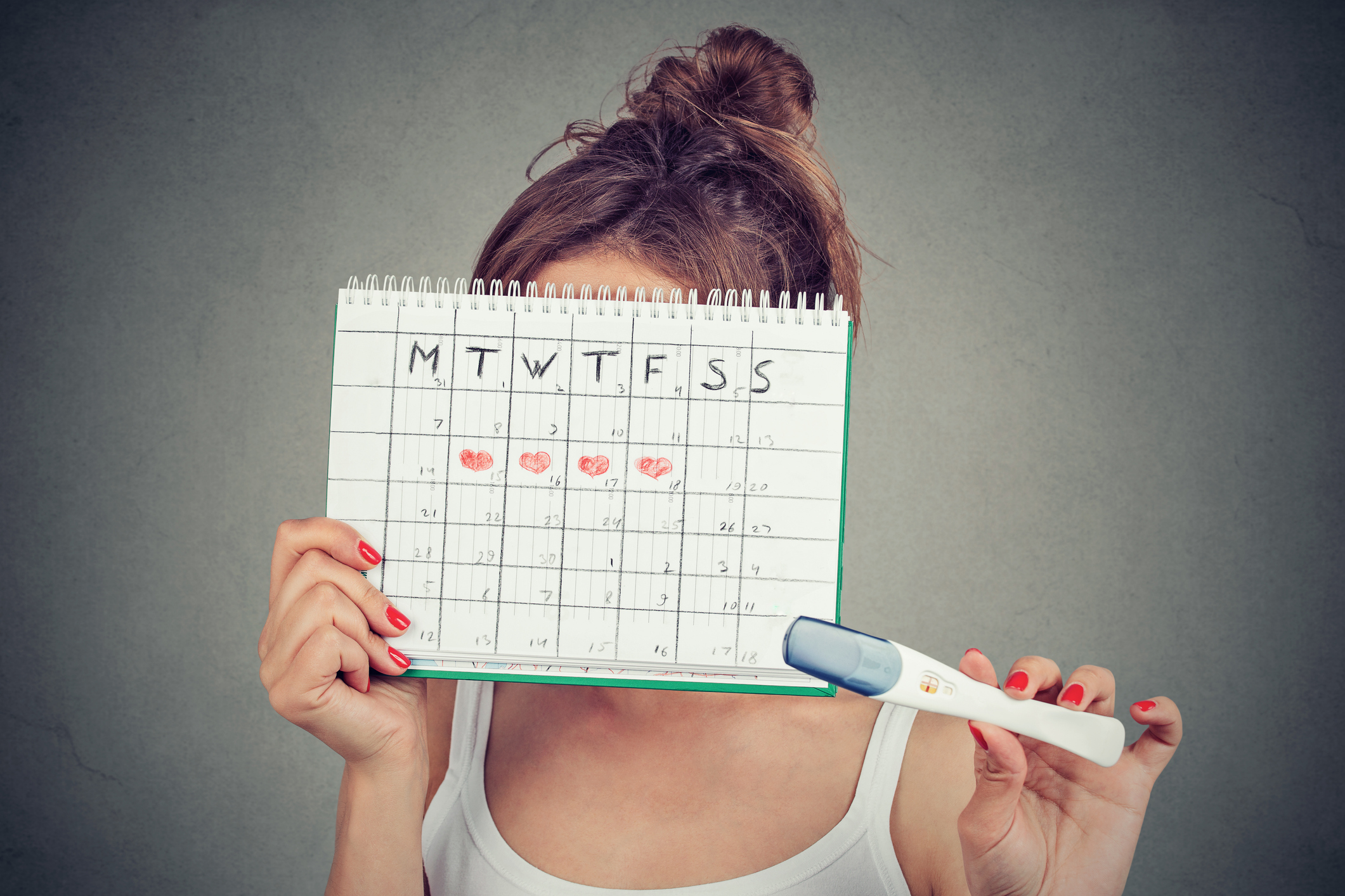 woman hiding behind a periods calendar and showing a positive pregnancy test