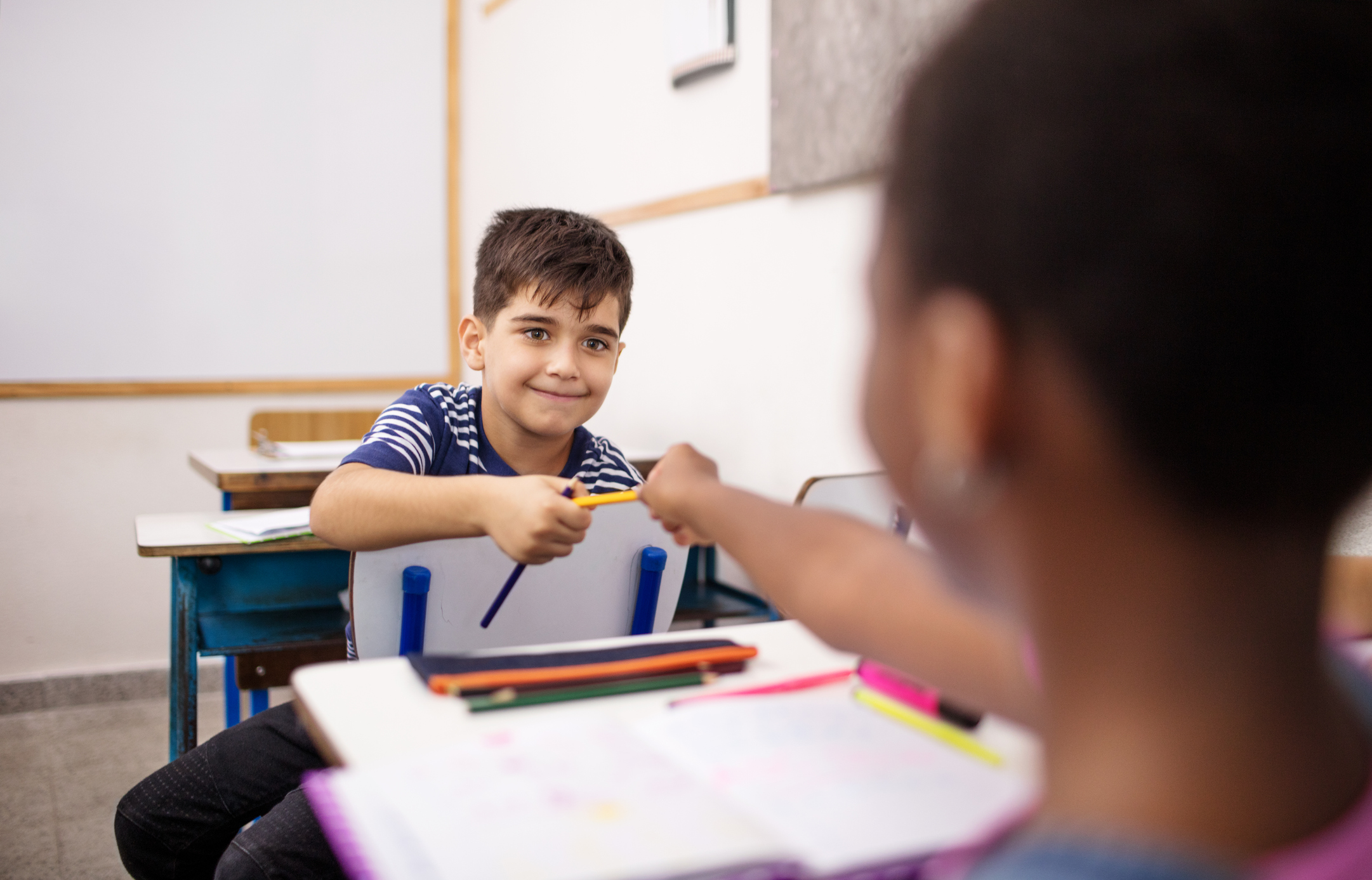 Schoolboy giving pencil to female friend in class