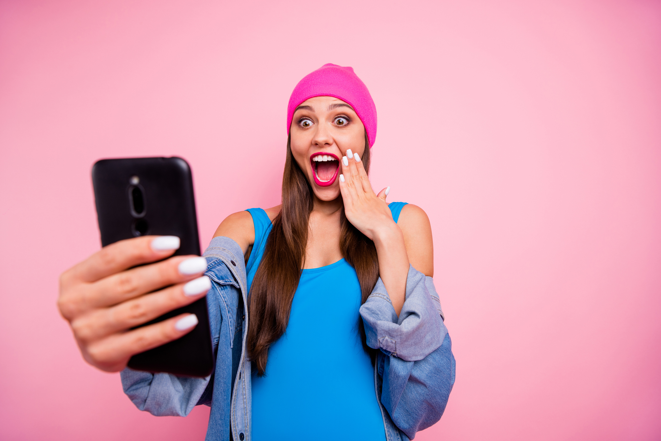 Portrait of impressed girl in body suit screaming wow omg touching her face isolated over pink background