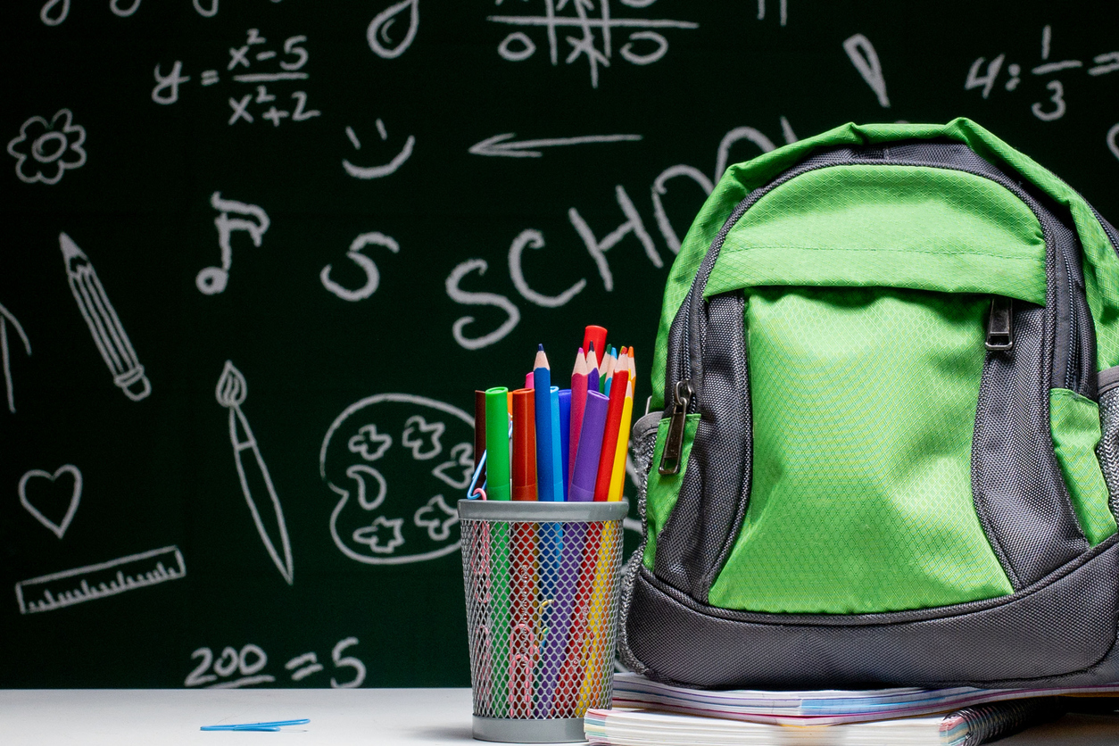 Education concept - green backpack, notebooks and school supplies on the background of the blackboard