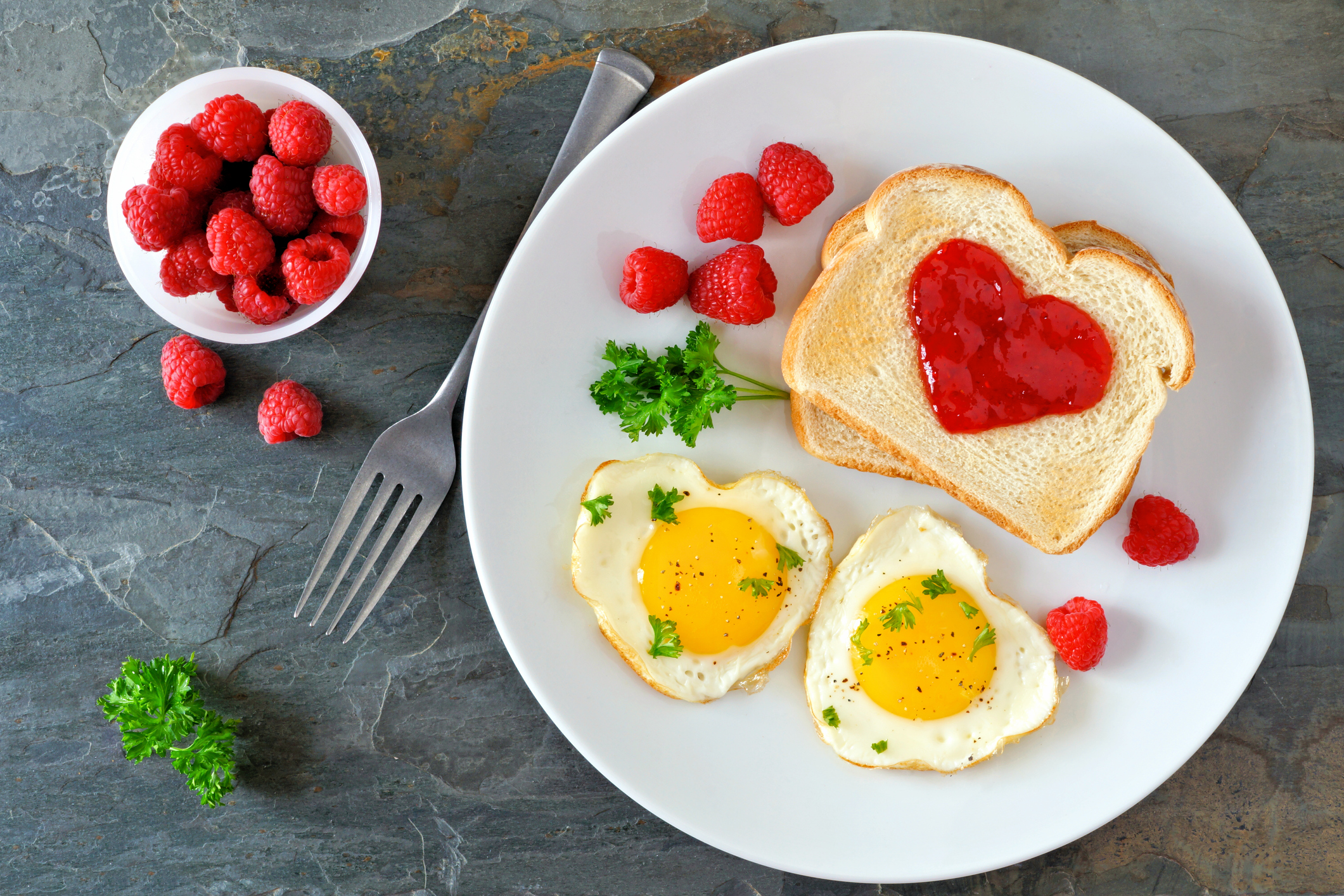 Valentines Day brunch with heart shaped eggs and toast with jam, above scene over a dark background