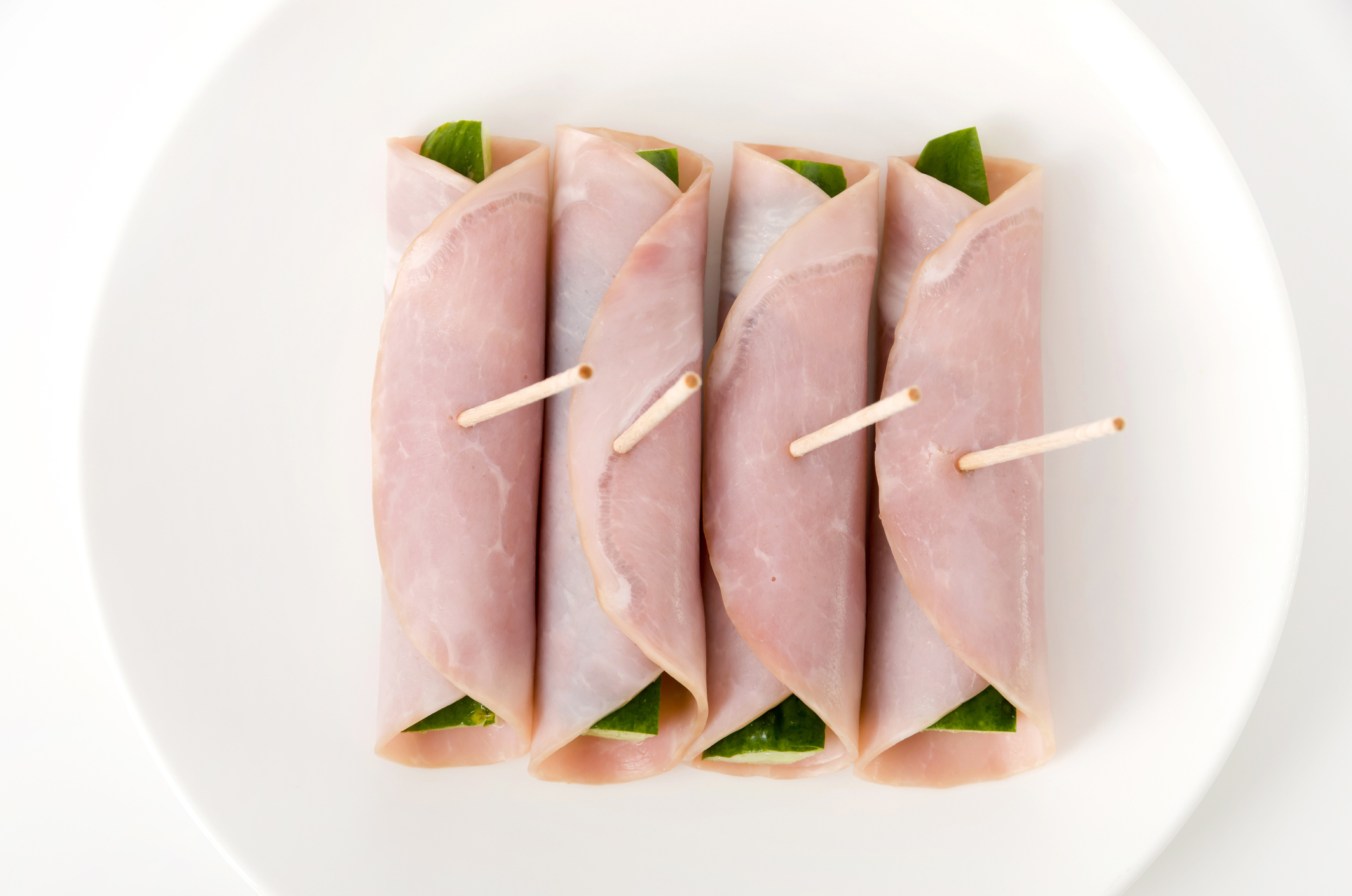 fresh Cucumber wrapped in loin ham on a dish on white background