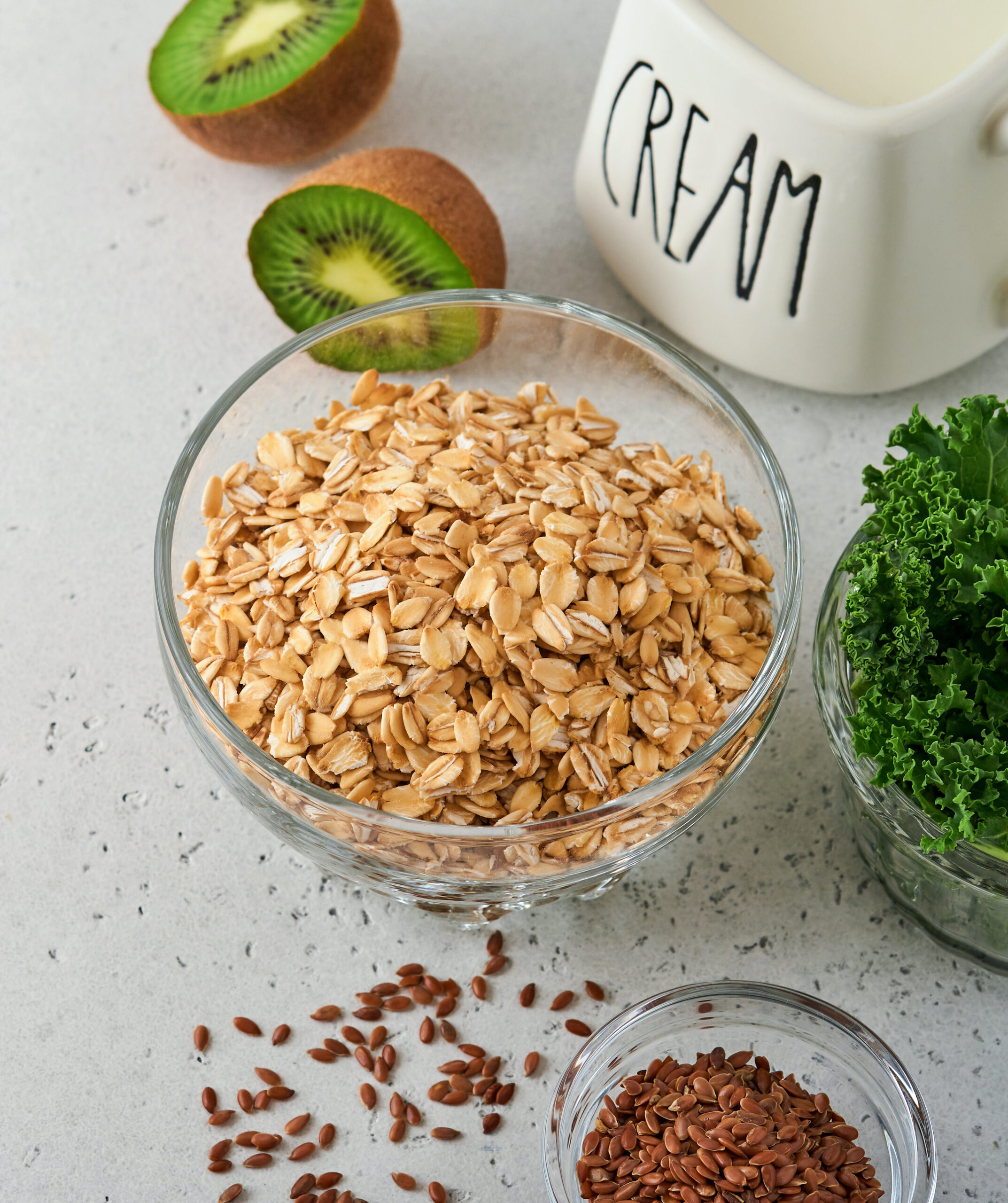 Oatmeal, kale, kiwi and chia seeds, cream ingredients for making detox smoothies on gray light concrete background. Selective focus. Mock up.