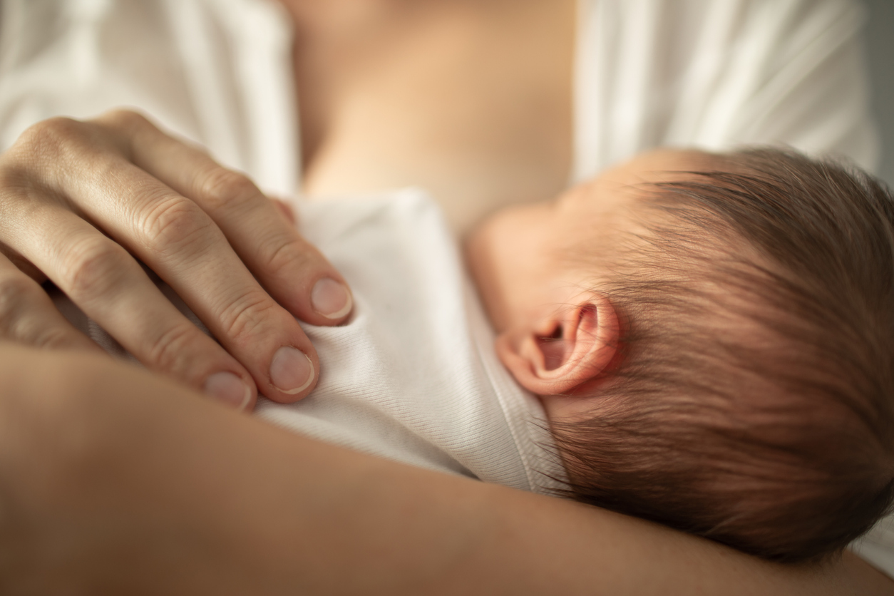 Newborn baby girl breast feeding in mothers arms.