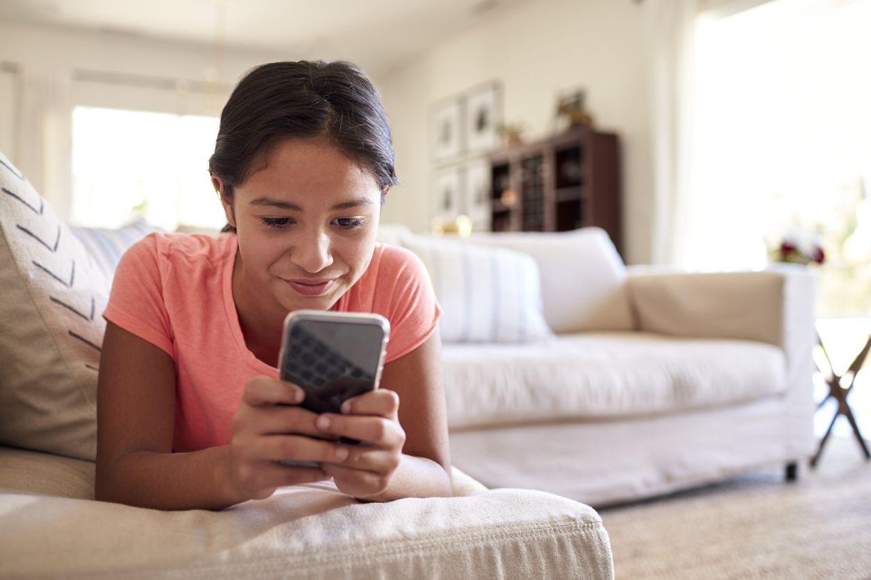 Teenage girl lying on the sofa at home in the living room using smartphone, close up, low angle, close up