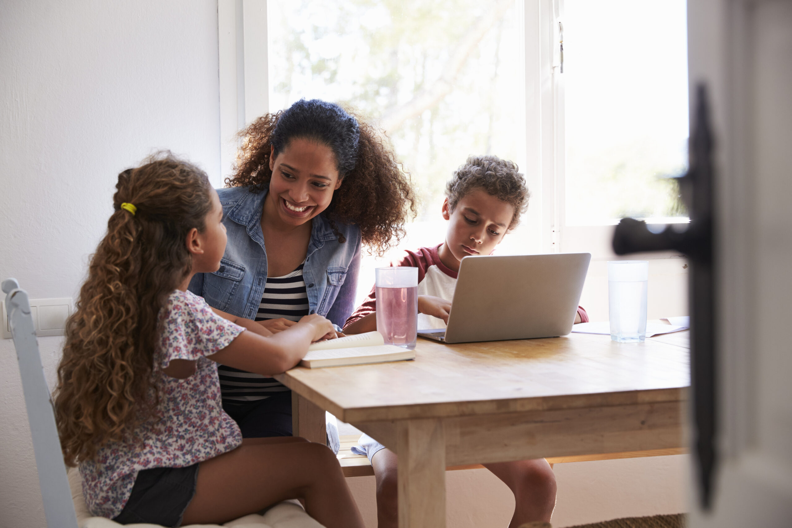 Mum sitting with kids at kitchen table, son using laptop