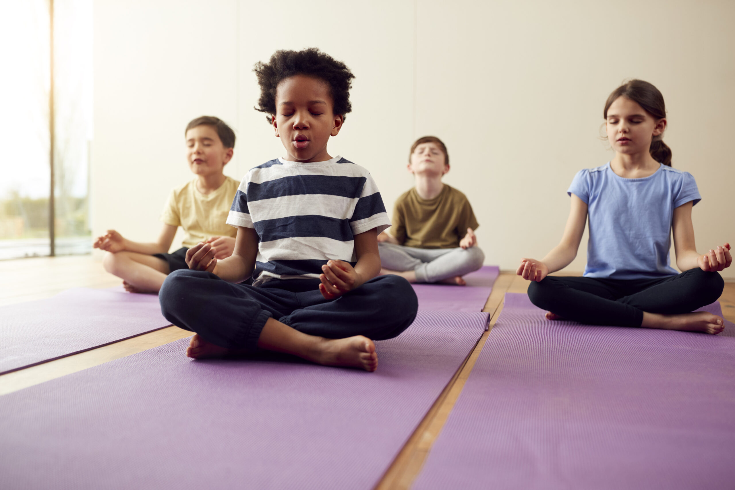 Group Of Children Sitting On Exercise Mats And Meditating In Yoga Studio