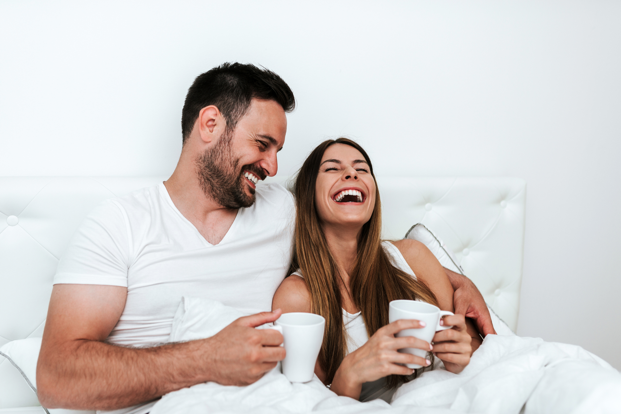 Happy couple having a cup of coffee or tea in the bed.