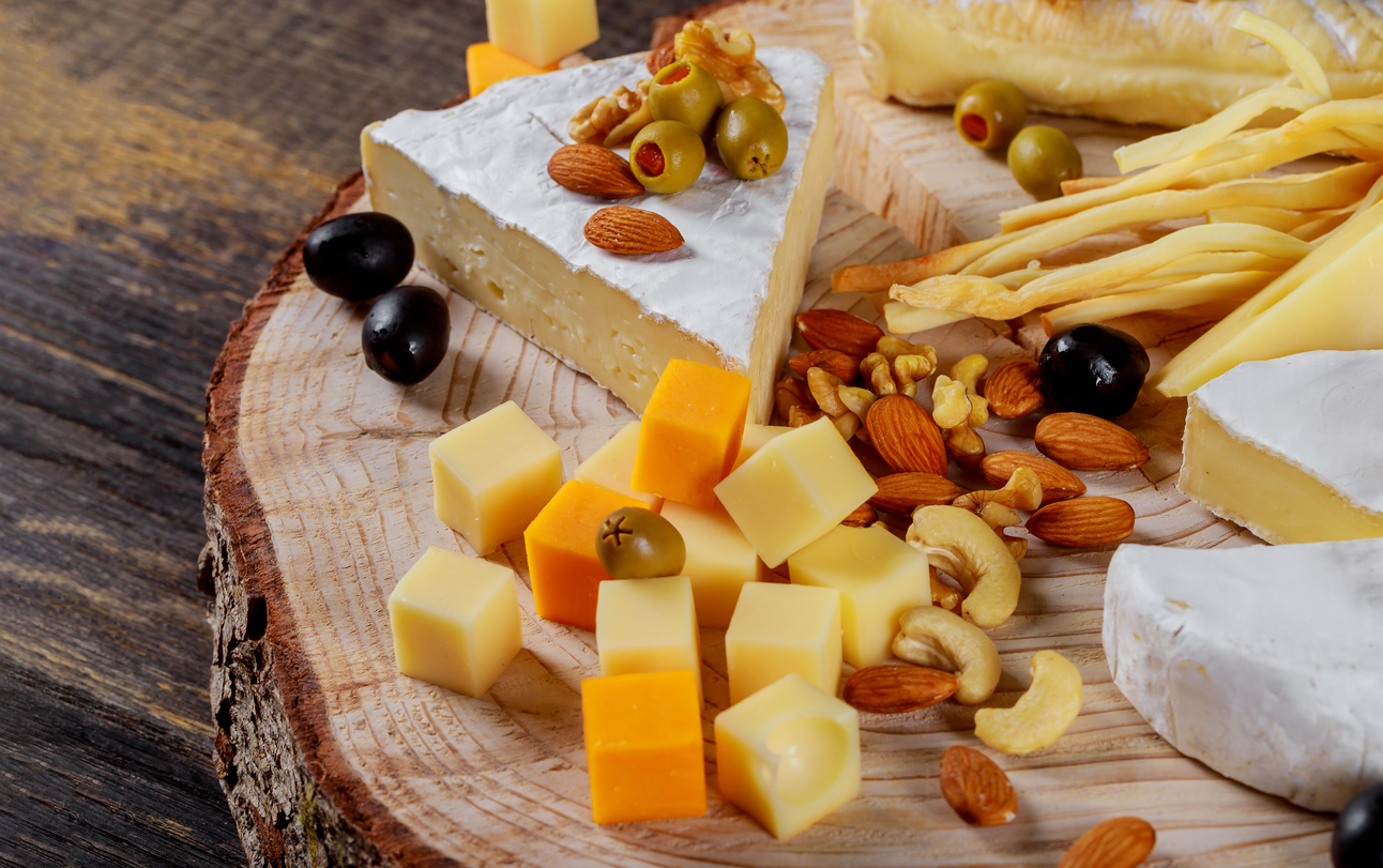 Different kinds of cheese, olives and assorted nuts wood background