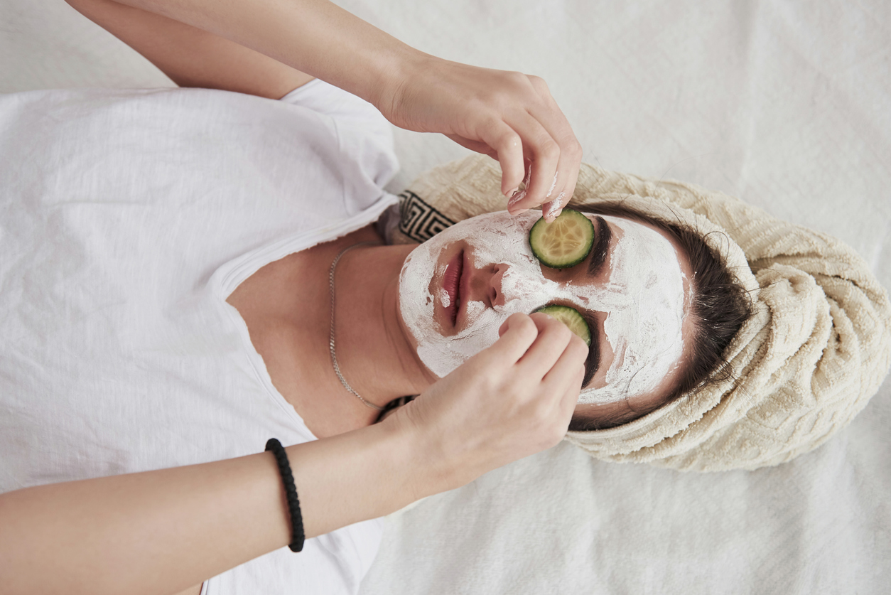 Top view of girl in white beauty mask on face and cucumber rings on eyes