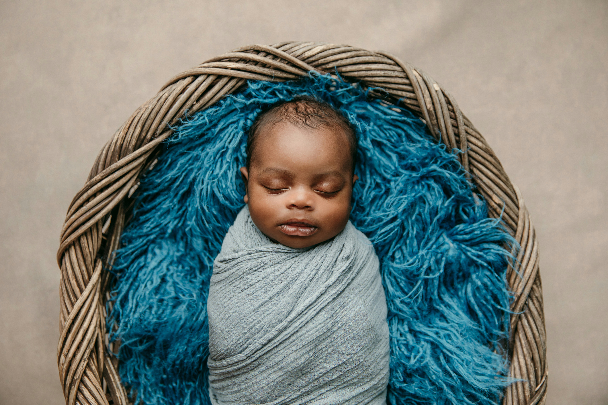 Sweet sleeping African-American newborn baby boy swaddled in a blanket and lying in a basket