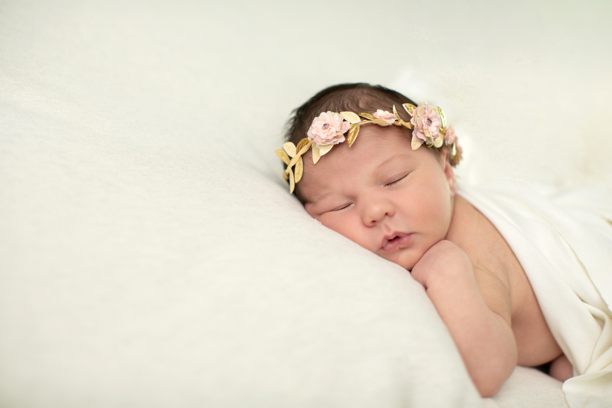 Sleeping newborn baby girl laying on a cream colored blanket with a floral crown on her head