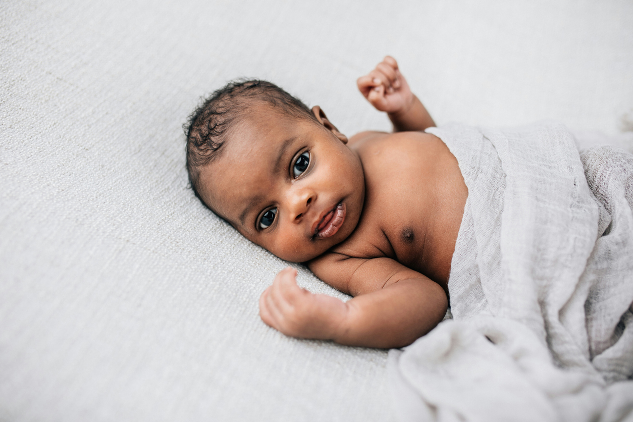 Beautiful African-American newborn little boy just a few weeks old swaddled in a cream colored soft blanket with copy space