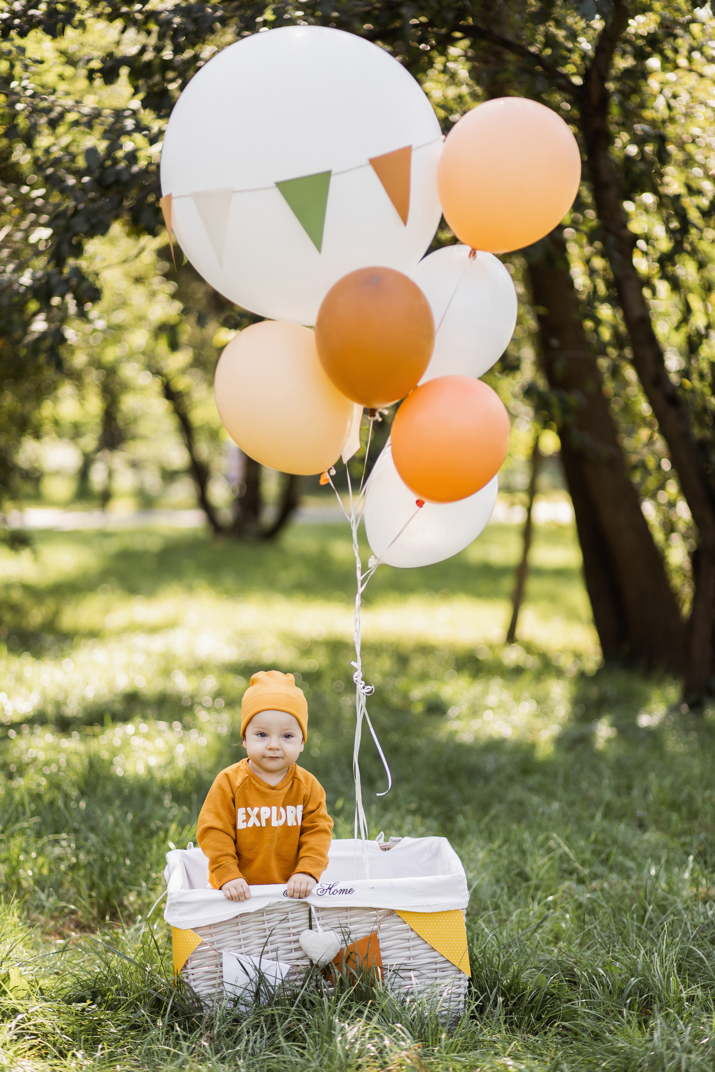 Playful little boy standing in wicker basket with balloons