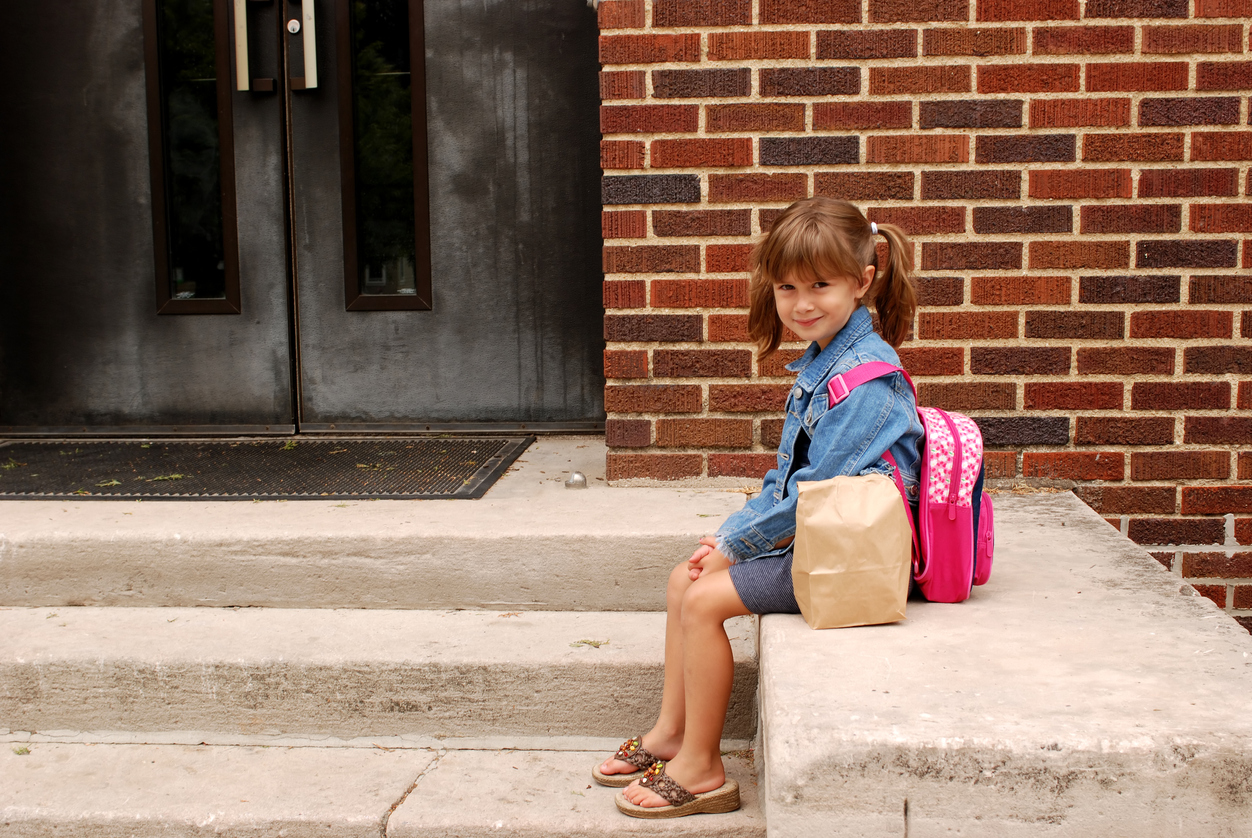 Little girl sitting outside with her backpack and snacks