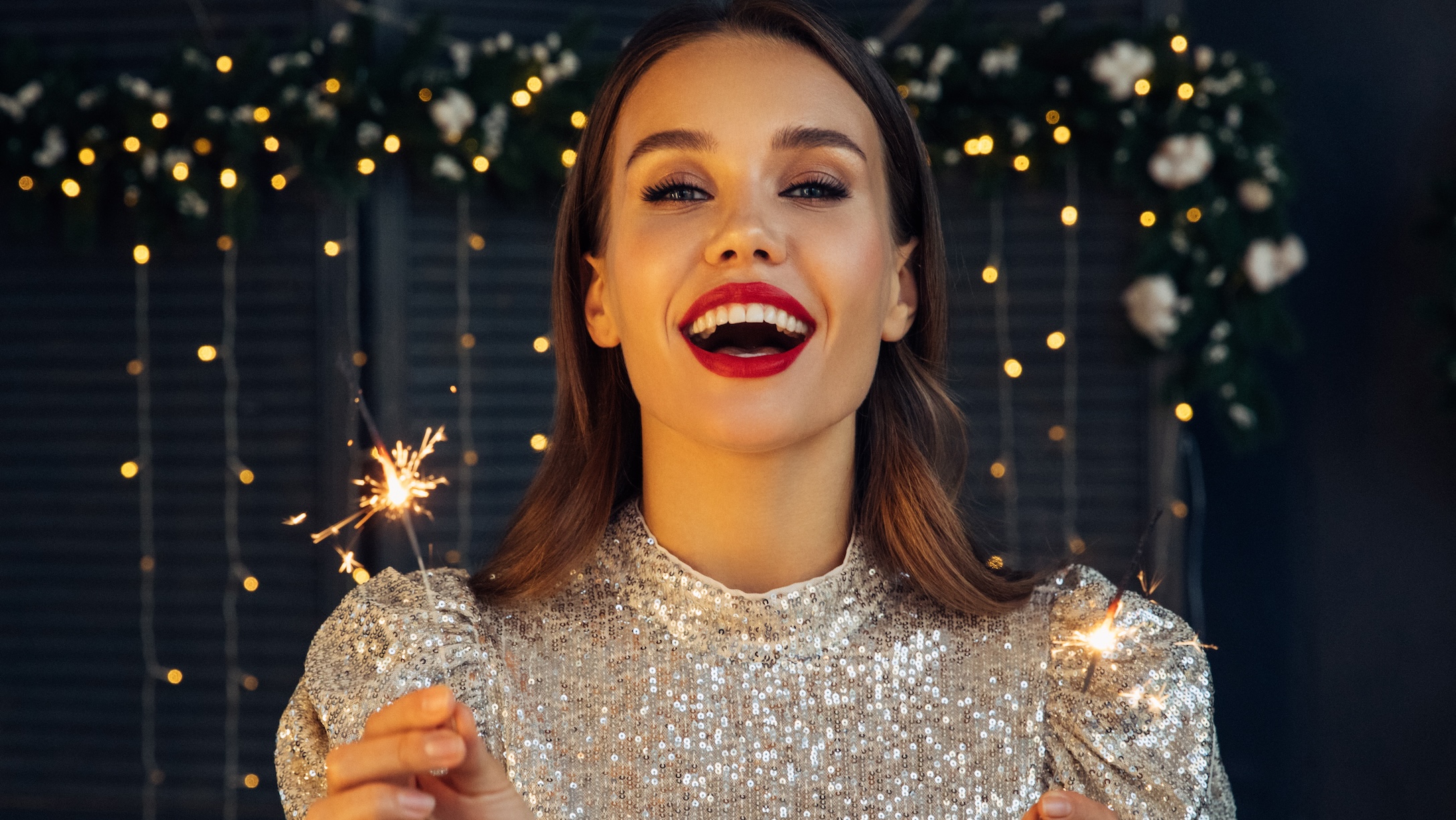 Happy beautiful woman holding festive sparkler among Christmas night