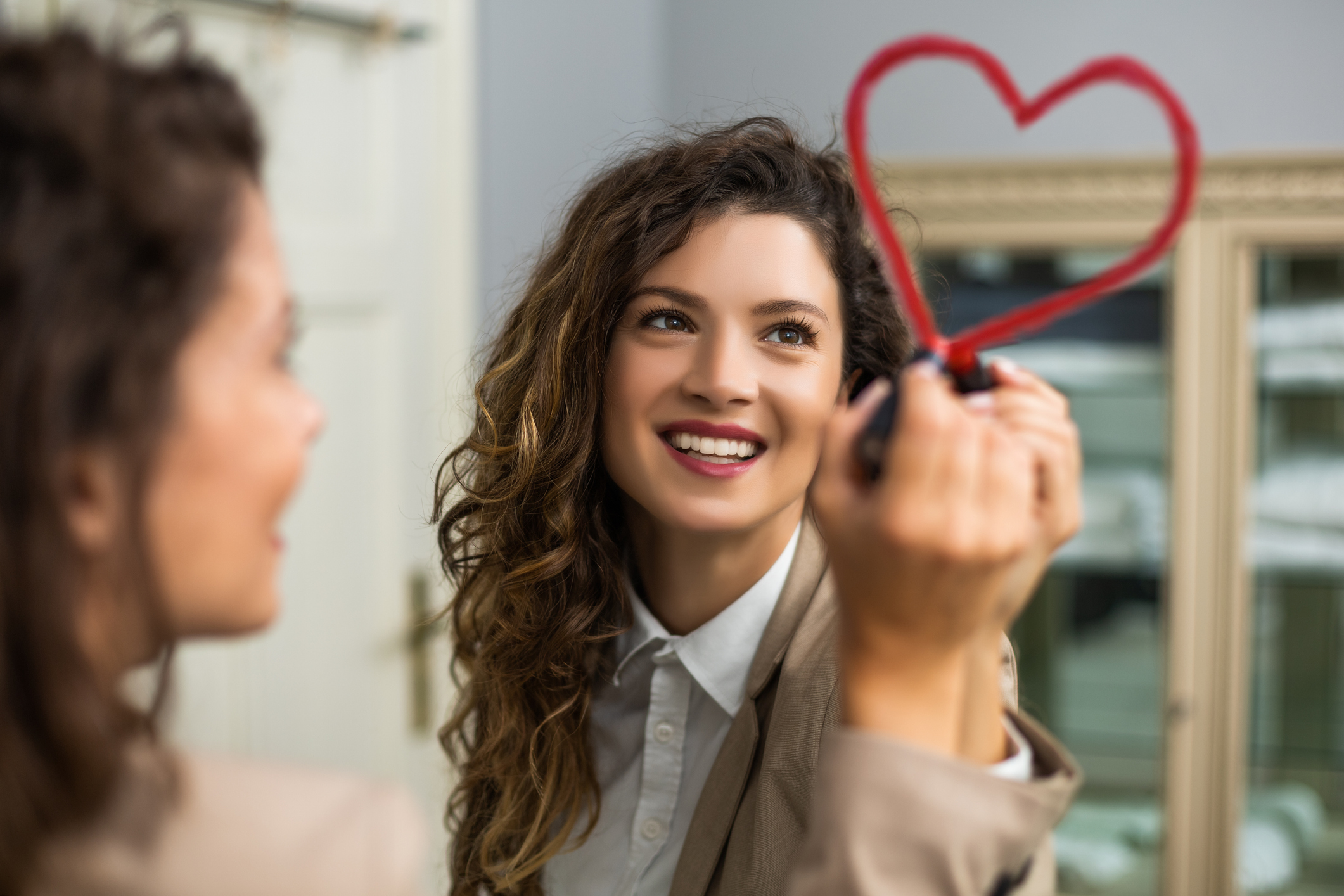 Woman drawing heart with lipstick on the mirror