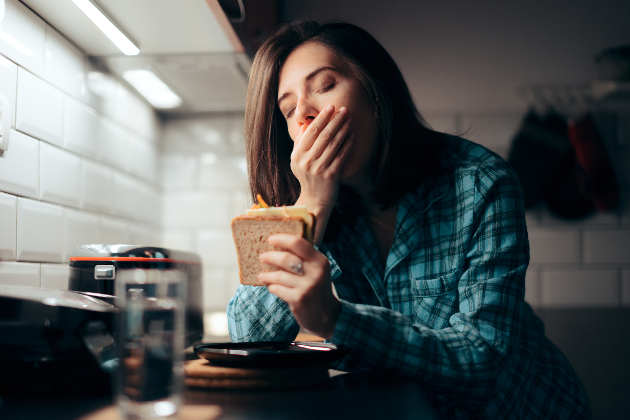 Sleepy Woman Holding a Sandwich in the Kitchen