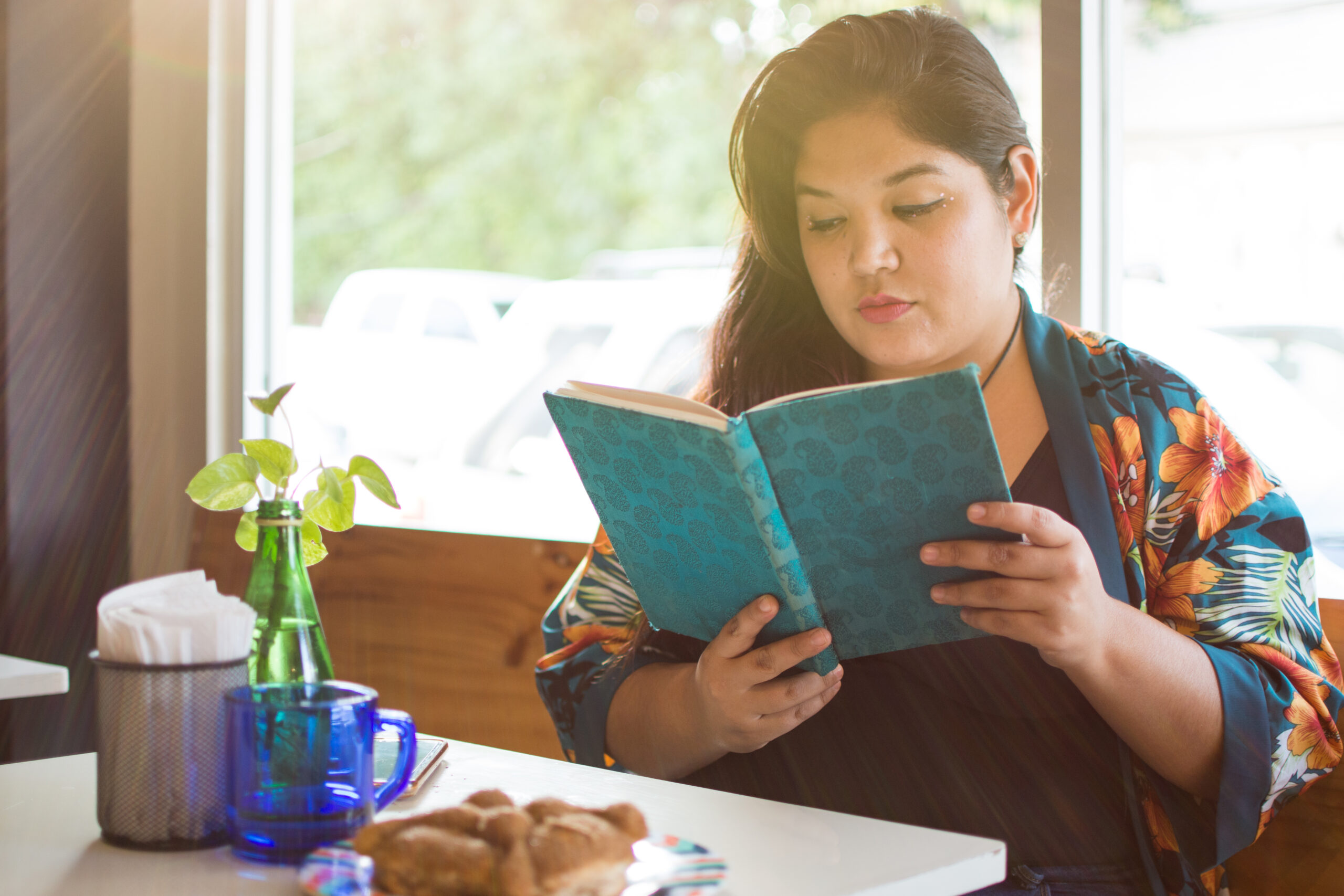 Latina young woman reading at a restaurant.