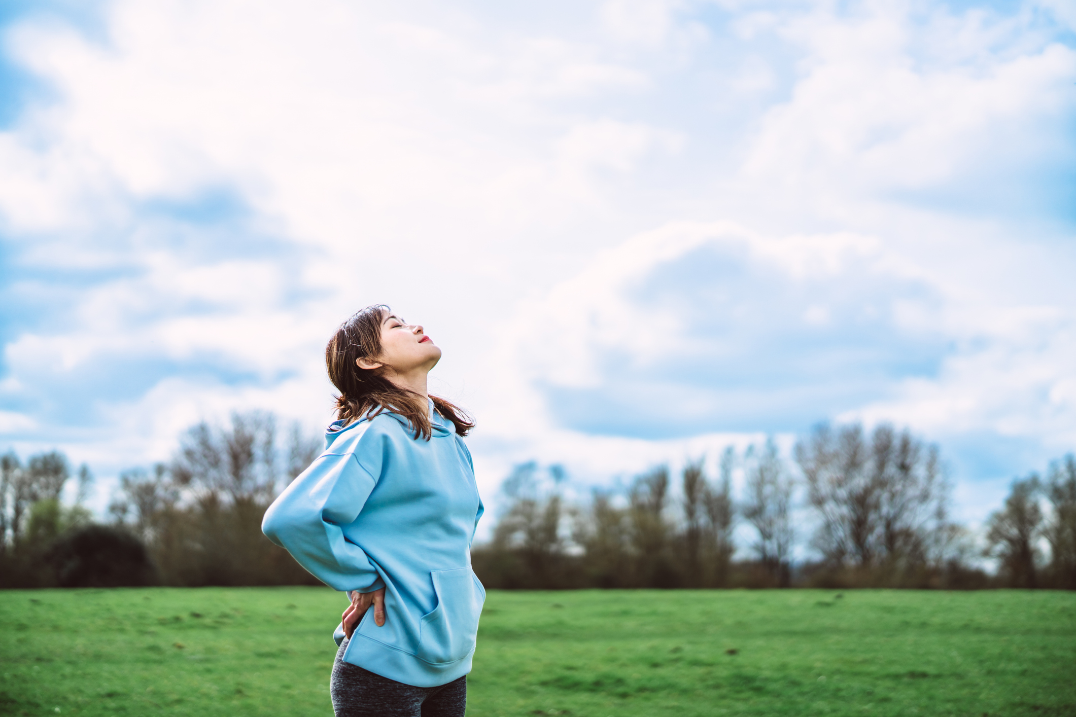 Beautiful cheerful Asian woman with positive expression relaxing and breathing for fresh air in nature