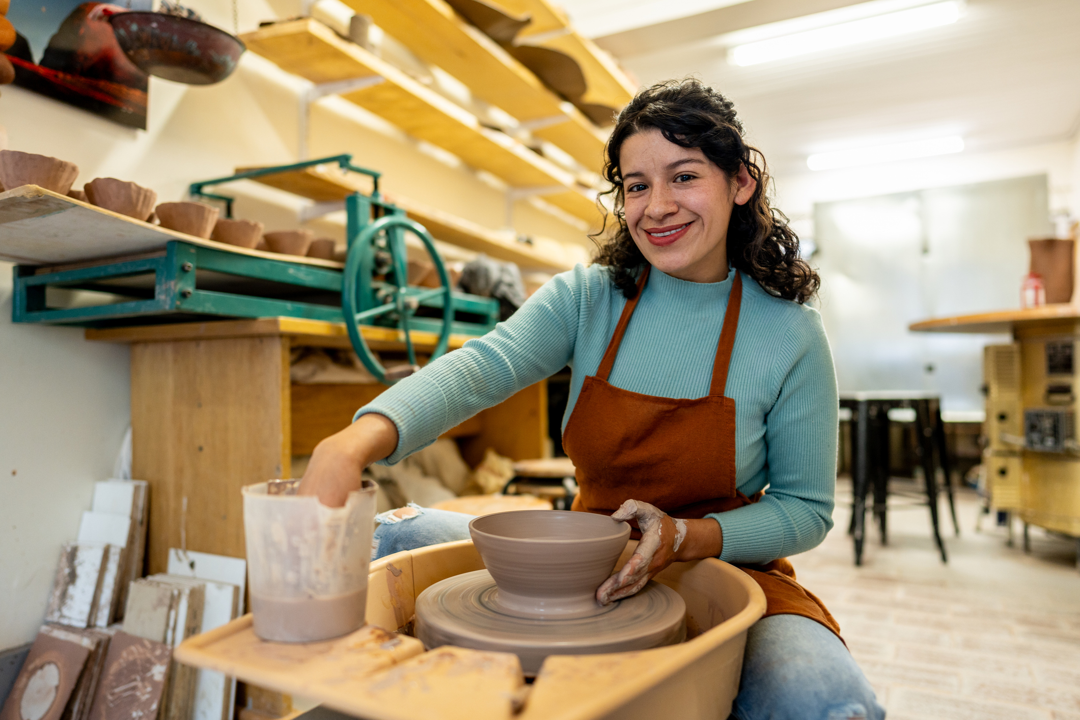 Portrait of a young woman molding clay on a pottery wheel at ceramics workshop