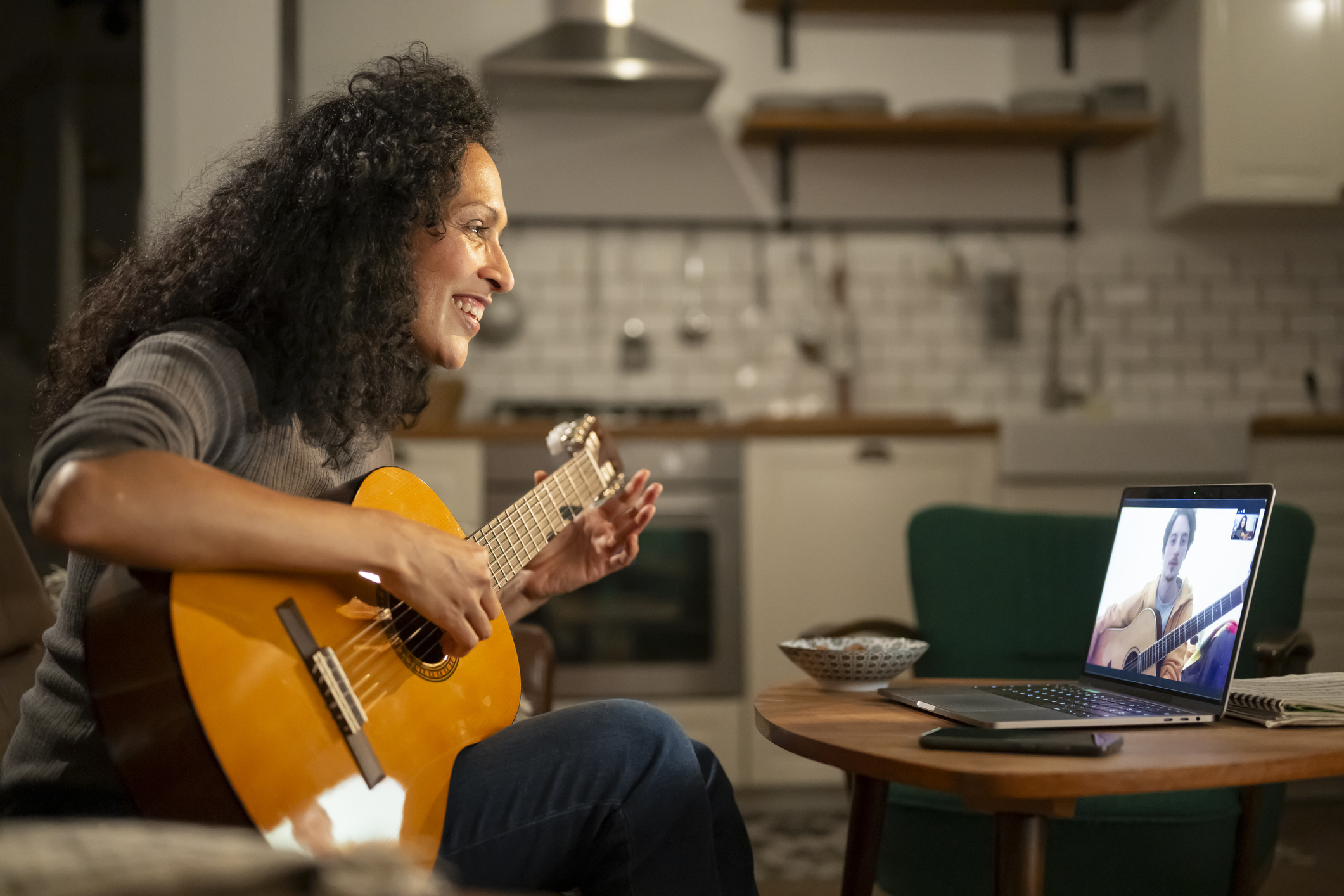 Woman playing guitar in front of laptop