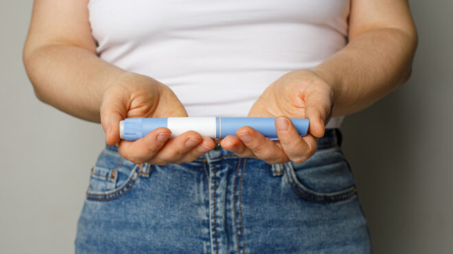 Blue Injection pen in female hand closeup. Semaglutide or insulin drug against female belly. Diabetes and Weight Loss concept.