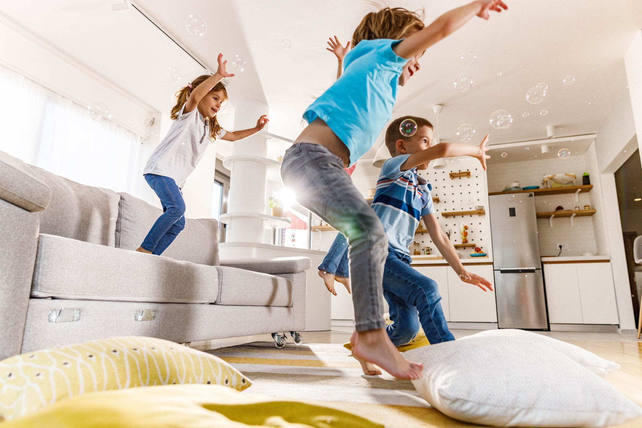 Playful kids having fun while jumping from sofa at home.