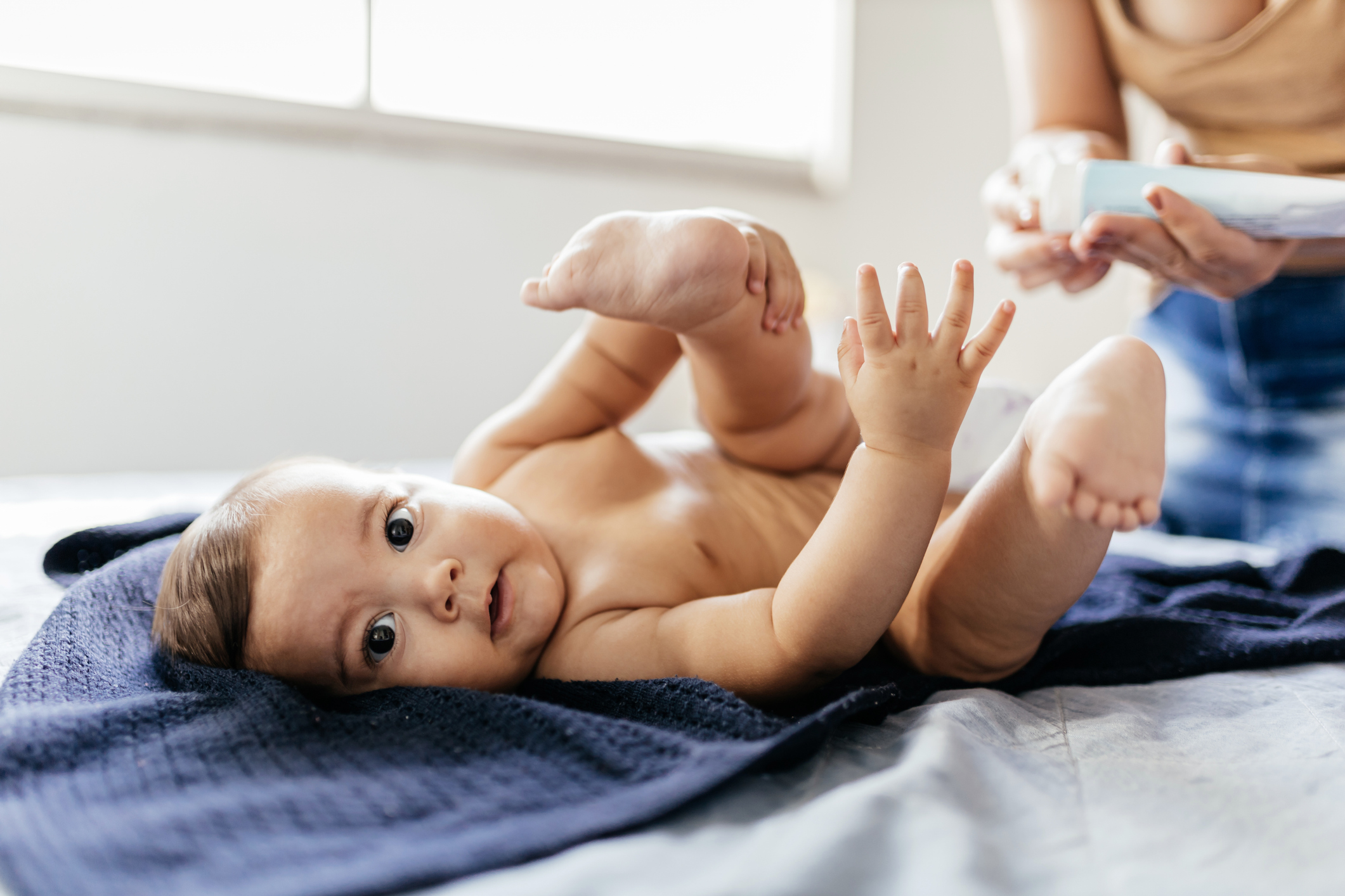 Mother changing baby's diaper in bed. Mother applies diaper rash cream.