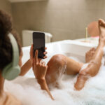 A woman bathes while using her phone, barefoot and barechested
