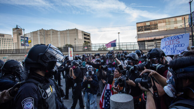 A protestor shouts at US Customs and Border Protection officers in riot gear