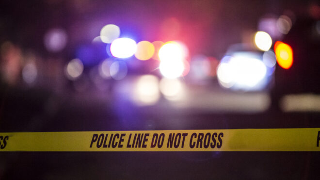 A crime scene is marked off by police crime scene tape, blurry background.